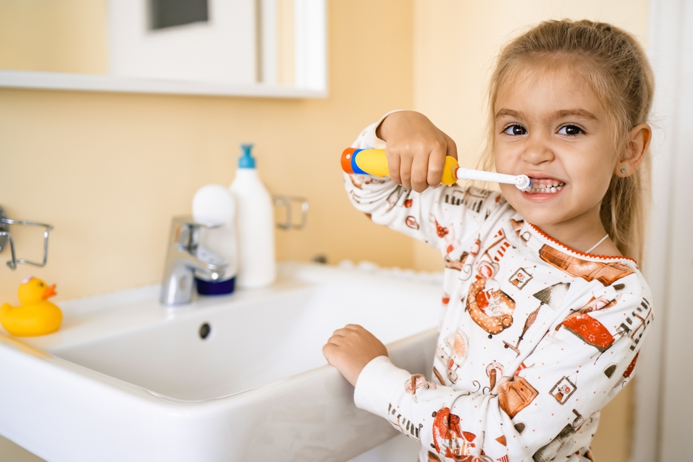 Child brushing teeth with electric toothbrush at bathroom sink, promoting dental hygiene and oral health for kids in context of juice impact on teeth.